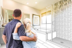 A man and woman stand in front of a bathroom in Long Beach, CA, examining a design sketch displayed on the wall, planning bathroom remodeling.