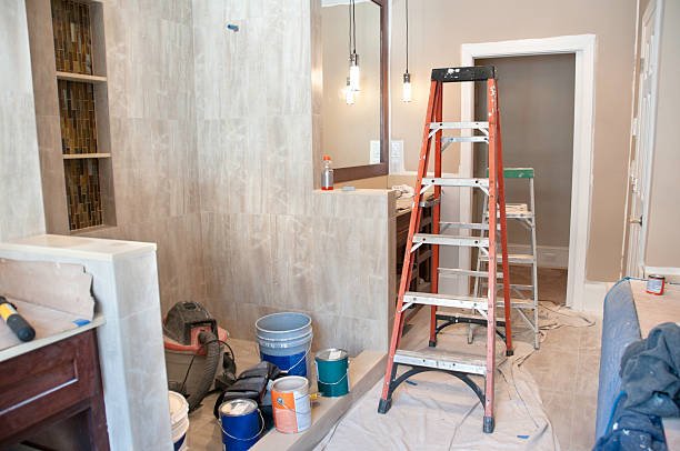 A man and woman stand in front of a bathroom in Long Beach, CA, examining a design sketch displayed on the wall, planning bathroom remodeling.