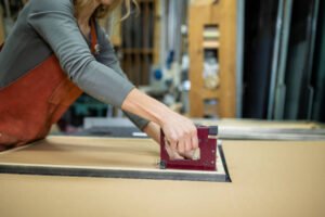 A woman operates a stapler to cut through a piece of cardboard, demonstrating a creative crafting technique | Framing service in Newport Beach, CA.