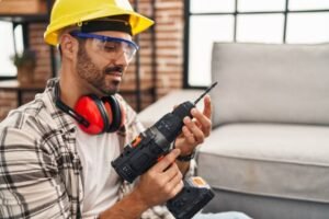 A man wearing a hard hat and safety glasses operating a drill on a construction site | Handyman service in Newport Beach, CA.