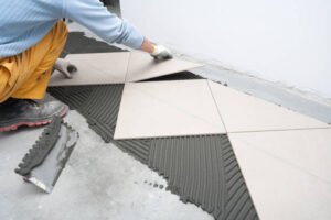 A man carefully lays tiles on the floor, focusing on precision and alignment in his work for tiles installation and repair in Long Beach, CA.