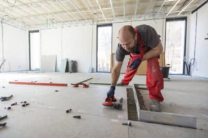 A man dressed in red overalls is engaged in floor work, demonstrating concentration and effort in tiles installation and repair in Long Beach, CA.