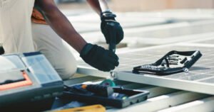 Handyman in Huntington Beach, CA, installing a solar panel on a rooftop, focusing intently on his work under clear blue skies.