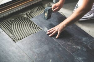 Tile installation and repair services in Newport Beach – a man using a hammer to secure floor tiles in a well-lit room.