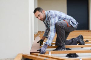 An experienced handyman providing affordable handyman services in Long Beach, carefully installing a wooden floor with tools and materials around him.