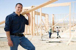 A confident man stands in front of a construction site, with cranes and building materials, representing expert framing contractors in Irvine, CA.